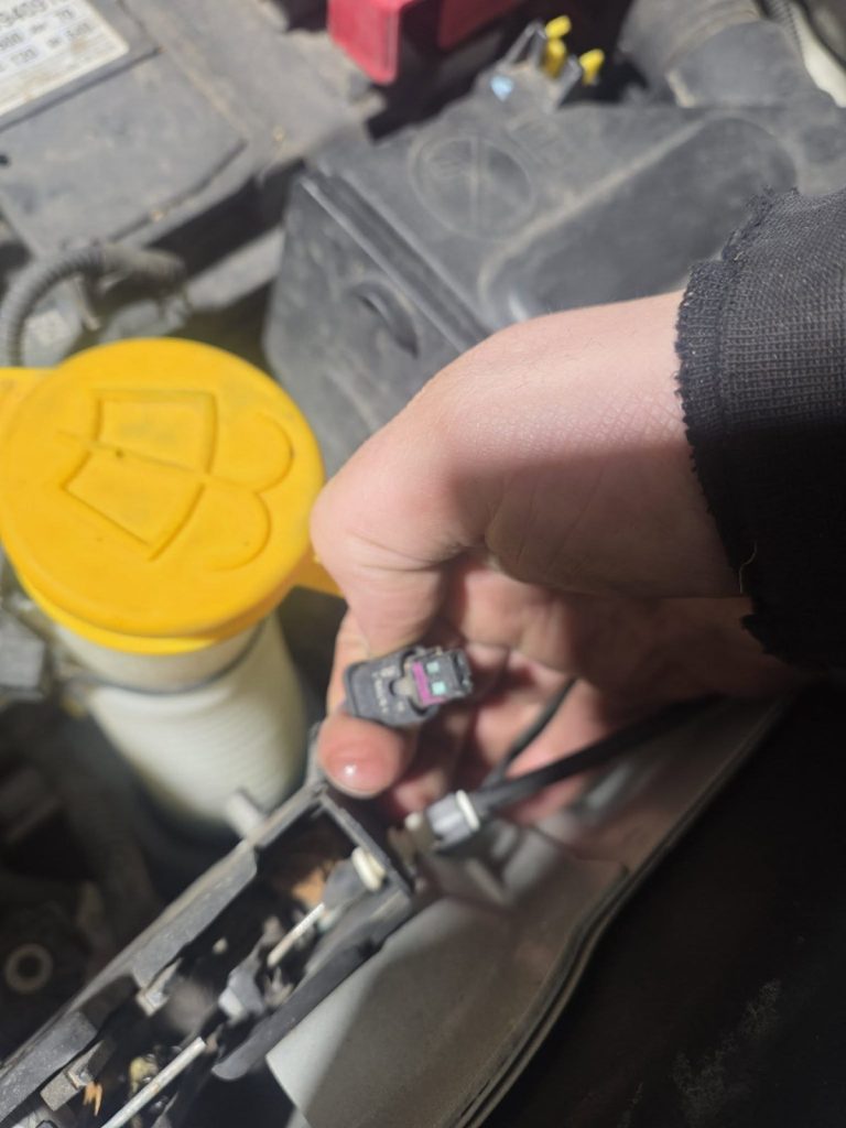 Technician holding an engine sensor connector during diagnostics at TinJToo Auto Repair
